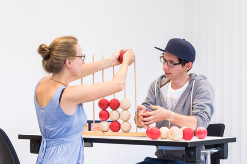 LEC48581_Vier gewinnt_Ergotherapie Ausbildung zum Ergotherapeuten: Patient und Therapeutin spielen "Vier gewinnt" in abgewandelter Form: Die Ergotherapeutin zeigt dem Patienten, wie die Kugeln über Stäbe gestetzt werden.