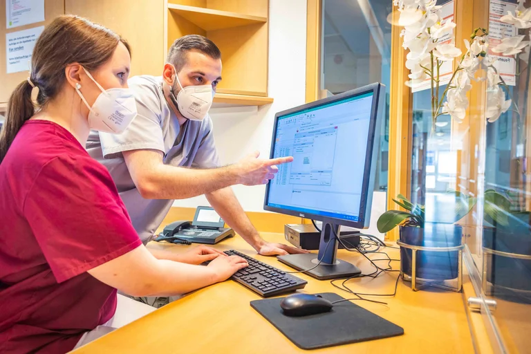 Altenpfleger Denis Reinecke unterstützt eine Auszubildende bei der Dokumentation.