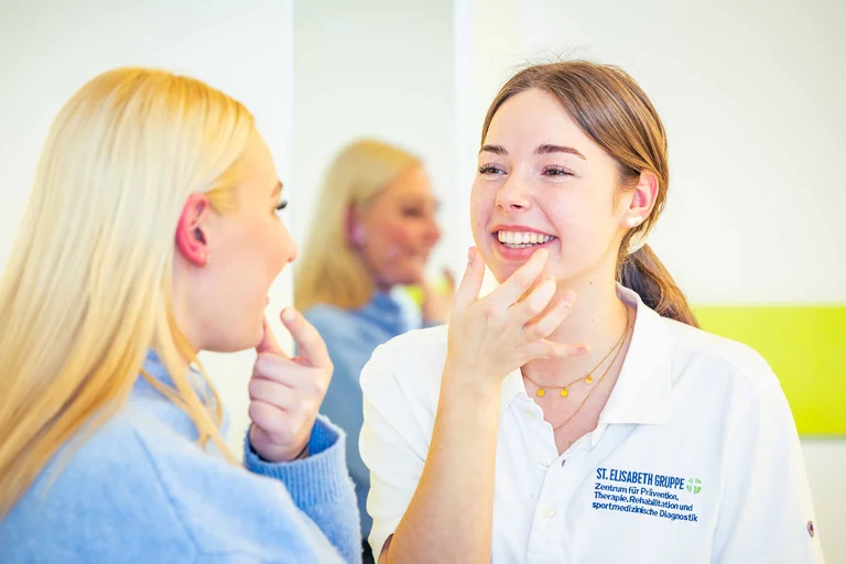 Eine Logopädie-Auszubildende erklärt einer Patientin wie sie ihren Mund formen soll