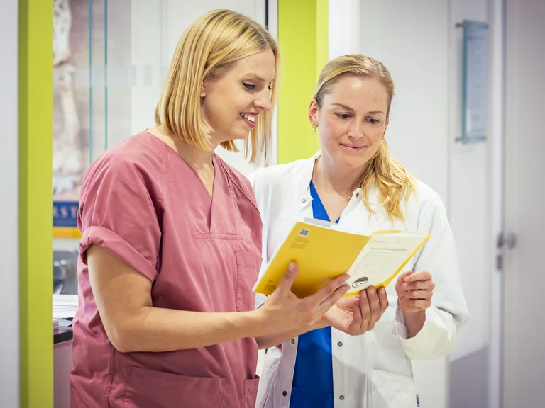 Eine Hebamme und eine Ärztin schauen auf Station gemeinsam in einen Mutterpass.