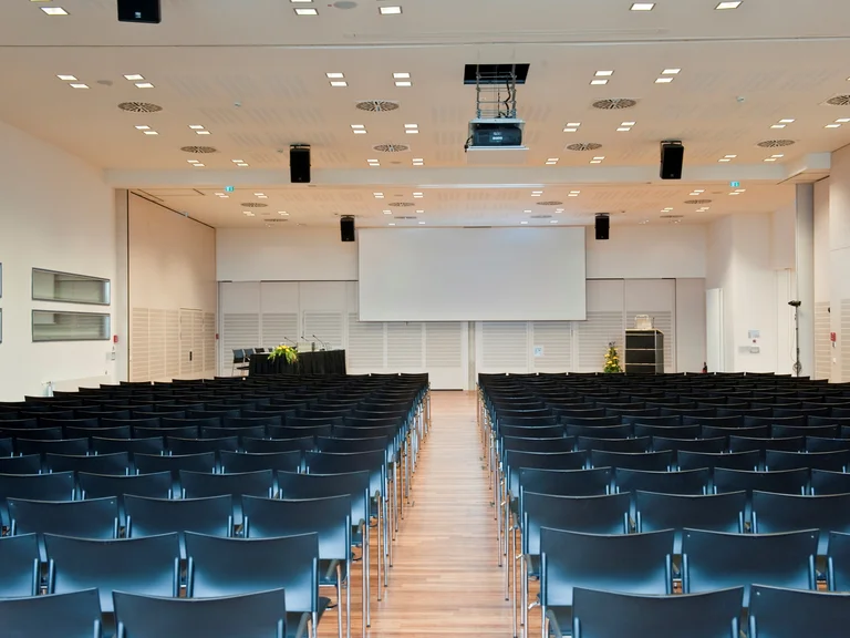 Kongresszentrum - Veranstaltungsraum mit Reihenbestuhlung und Beamerleinwand