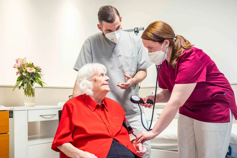 Praxisanleitung: Eine Auszubildende misst unter der Anleitung von Altenpfleger Denis Reineck den Blutdruck einer Bewohnerin.