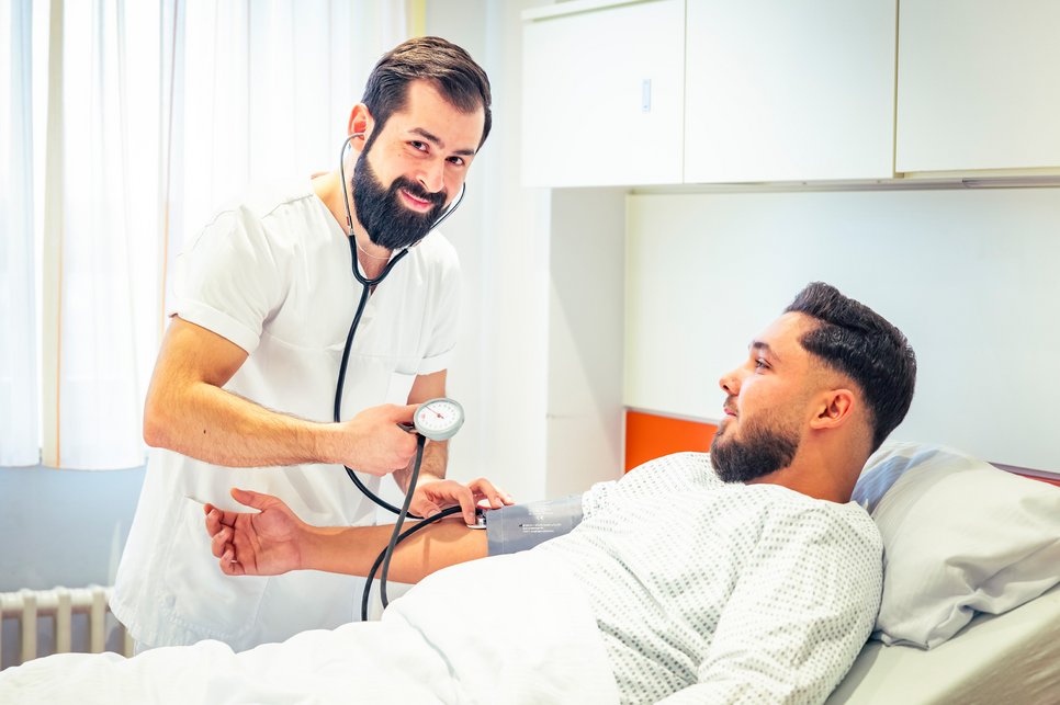 Blutdruck messen Das Bild zeigt einen Pflegefachassistenten, der bei einem Patienten Blutdruck misst.