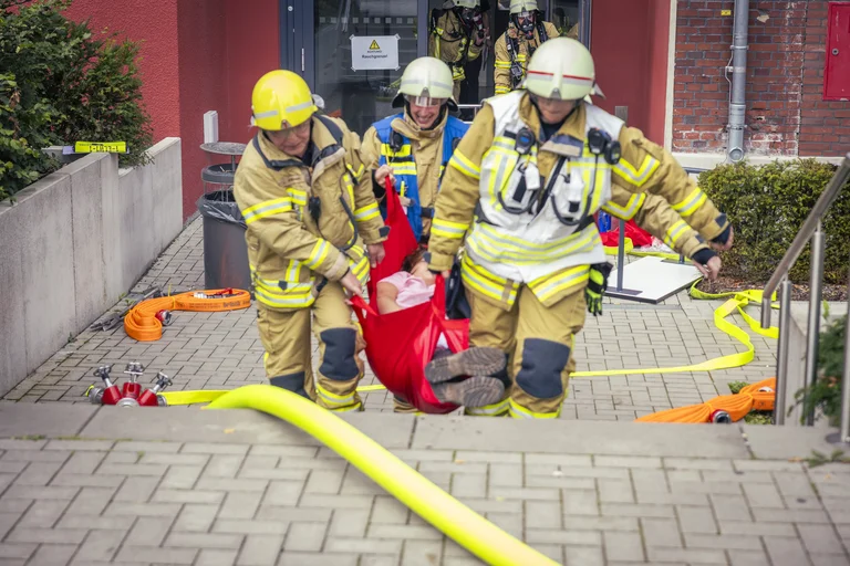 Feuerwehrleute tragen eine Verletzte aus einem Gebäude
