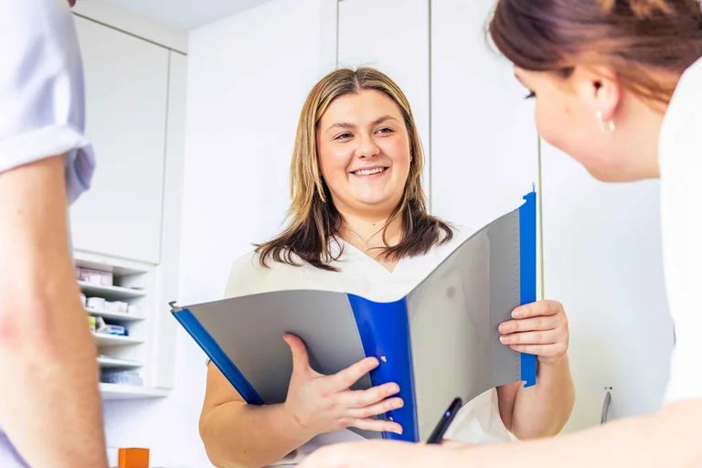 Bild zeigt einen Berufseinblick: Frau mit Heft schaut zwei Mitarbeiter an