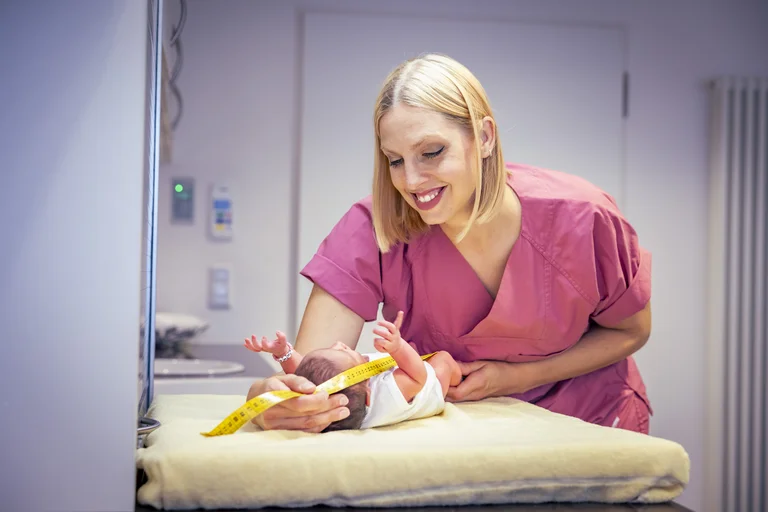 Eine Hebamme misst den Körper eines neugeborenen Babys mit einem Maßband