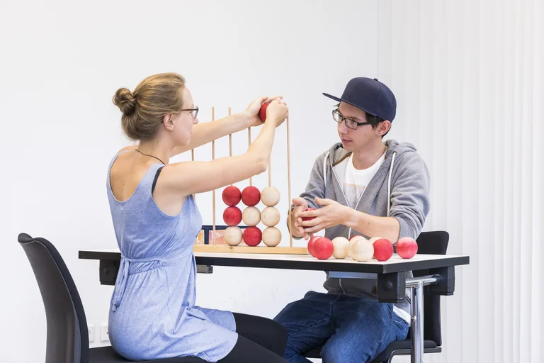 Ausbildung zum Ergotherapeuten: Patient und Therapeutin spielen "Vier gewinnt" in abgewandelter Form: Die Ergotherapeutin zeigt dem Patienten, wie die Kugeln über Stäbe gestetzt werden. 