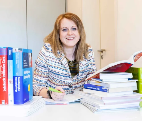 Bachelorabsolventin am Arbeitsplatz: Nach dem Pflegestudium ist die junge Frau auf dem Bild als Pflegewissenschaftlerin in der St. Elisabeth Gruppe aktiv. Hier auf dem Bild am Schreibtisch mit Büchern.