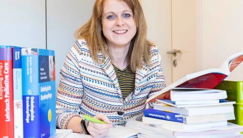 Bachelorabsolventin am Arbeitsplatz: Nach dem Pflegestudium ist die junge Frau auf dem Bild als Pflegewissenschaftlerin in der St. Elisabeth Gruppe aktiv. Hier auf dem Bild am Schreibtisch mit Büchern.