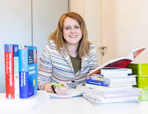 Bachelorabsolventin am Arbeitsplatz: Nach dem Pflegestudium ist die junge Frau auf dem Bild als Pflegewissenschaftlerin in der St. Elisabeth Gruppe aktiv. Hier auf dem Bild am Schreibtisch mit Büchern.